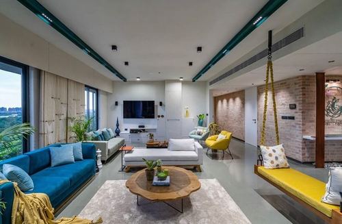Open living room with blue velvet sofa, round wood coffee table, and hanging swing by brick wall