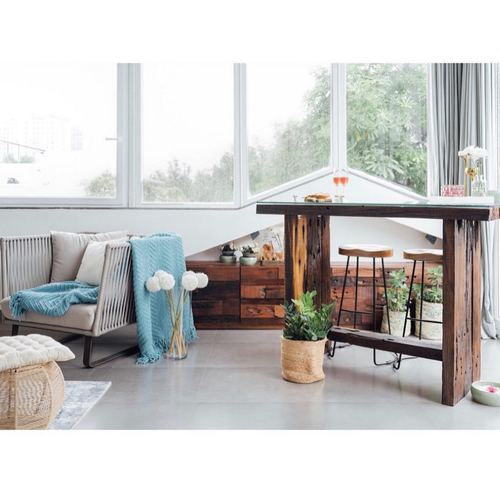 Terrace lounge with reclaimed wood bar table, bar stools, teal throw, and floor-to-ceiling windows