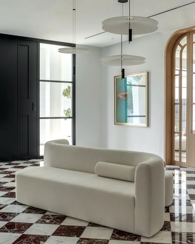 Entrance hall with curved cream sofa on burgundy and white checkered marble floor, disc pendants above