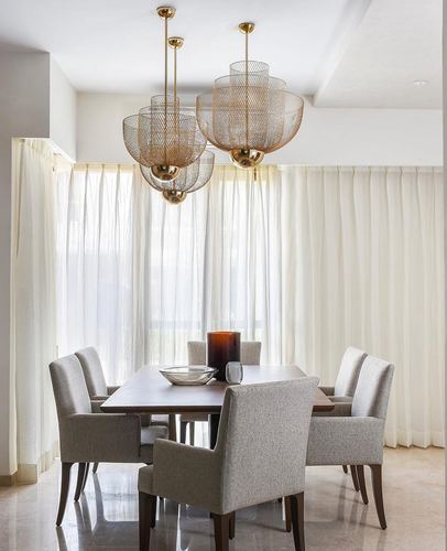 Dining room with sheer curtains, brass cage pendant lights, wood table and grey upholstered chairs