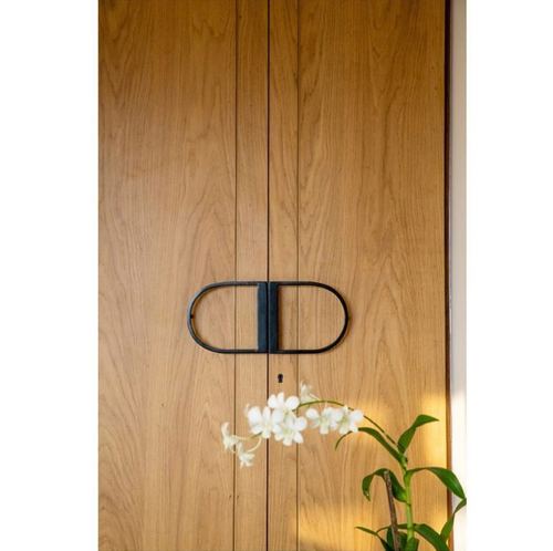 Close-up of a wood paneled door with a black capsule handle and white orchid in foreground