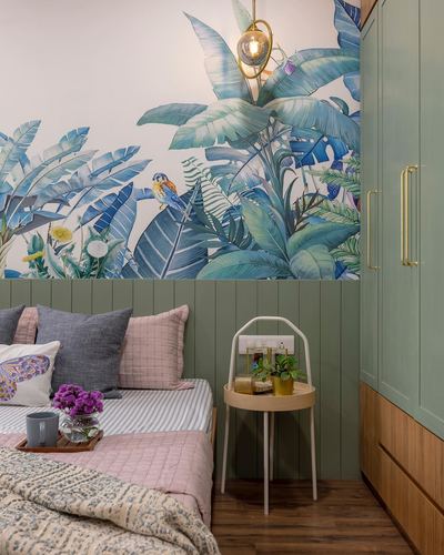 Bedroom corner with tropical leaf mural, green paneled wardrobe, round side table and pink-toned bedding