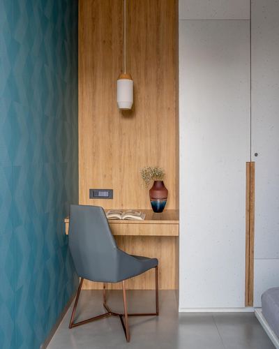Small wooden study nook with floating desk, grey chair, pendant light and teal patterned wall.
