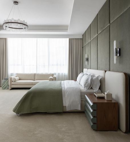 Bedroom with green upholstered headboard wall, wood nightstand, cream sofa, and sheer curtained window