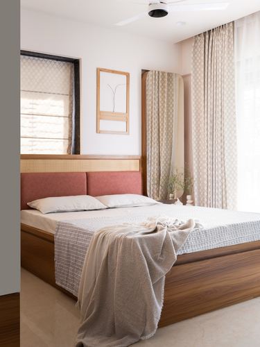 Bedroom with cane and pink upholstered headboard, wooden bed, patterned curtains and soft morning light