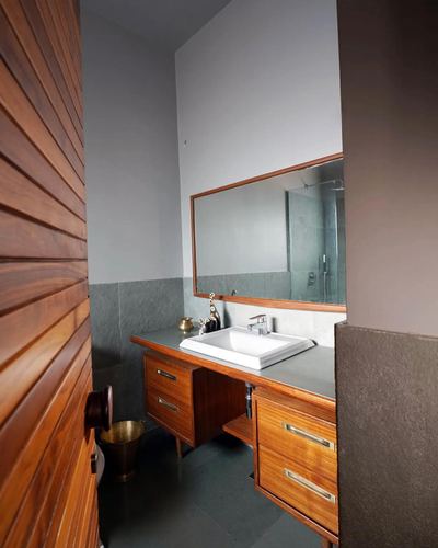 Wooden vanity with white sink beneath a wood-framed mirror in a stone-tiled bathroom