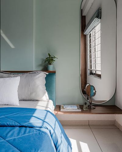 Bedroom corner with blue bedding, teal headboard, plant, and oversized oval mirror by window