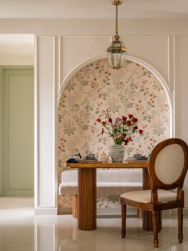 Dining nook in arched floral-wallpapered niche with wood table, cane bench, and brass lantern pendant.