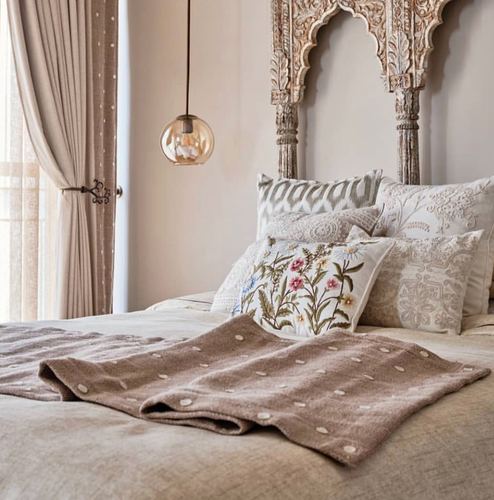 Bed with carved arched wooden headboard, layered pillows, and amber pendant light