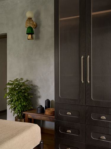 Dark wood wardrobe beside textured wall with mushroom-shaped sconce and potted plant in bedroom corner
