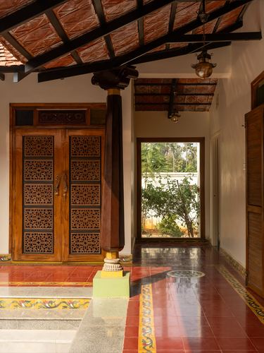 Chettinad-style entryway with carved wooden door, tiled floor, and view to garden through corridor