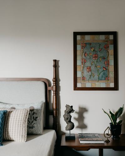Bedroom corner with carved wood bedpost, framed floral art, and bronze figurine on bedside table
