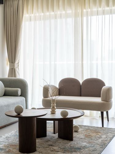 Curved taupe settee and round wood coffee tables in front of sheer curtained window