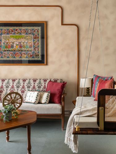 Living room corner with framed folk art, patterned sofa, and hanging cane swing