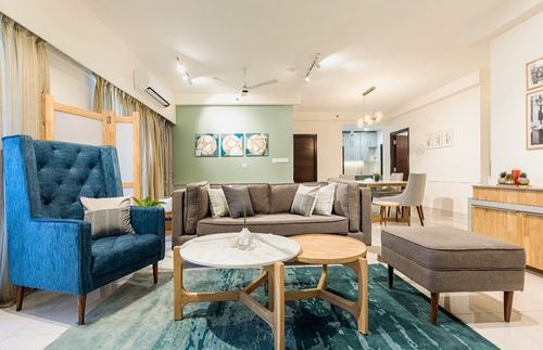Open-plan living room with blue tufted chair, grey sofa, round coffee tables and teal rug