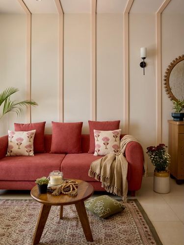 Terracotta sofa with printed cushions against a paneled cream wall, round mirror and wooden table nearby
