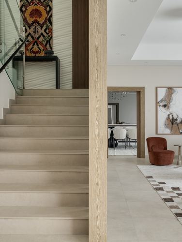 Stone staircase beside wood column opening into living room with rust armchair and dining beyond
