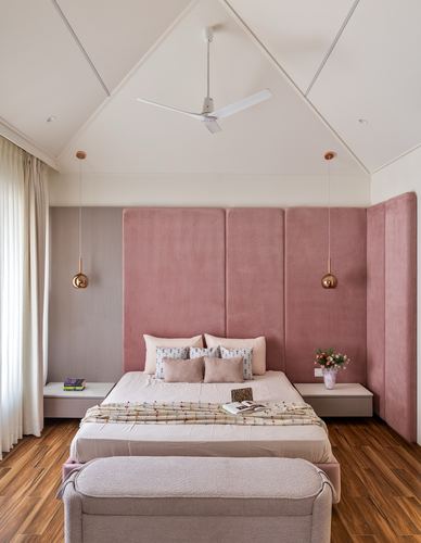Bedroom with vaulted ceiling, pink velvet headboard panels, wood floor, and copper pendant lights flanking the bed