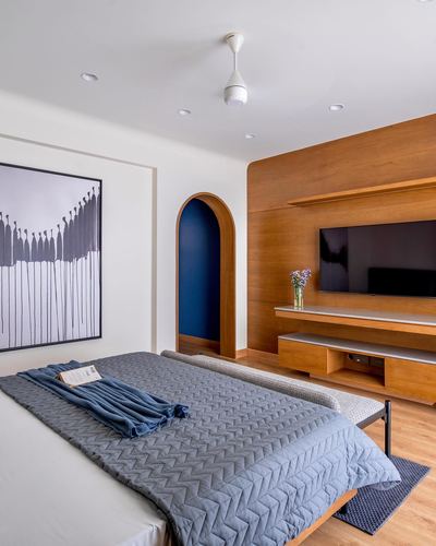 Bedroom with wood-panelled tv wall, arched blue doorway, grey quilted bed, and graphic wall art