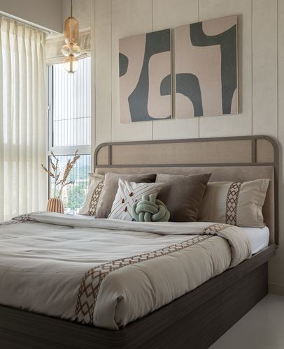 Bedroom with cane headboard, layered neutral bedding, and abstract wall art beside a window