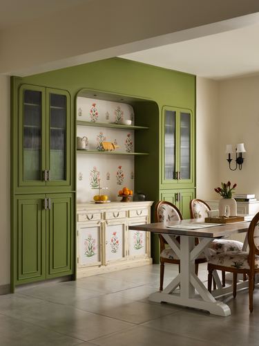 Green built-in cabinetry with hand-painted floral crockery niche beside a dining table with floral-upholstered chairs