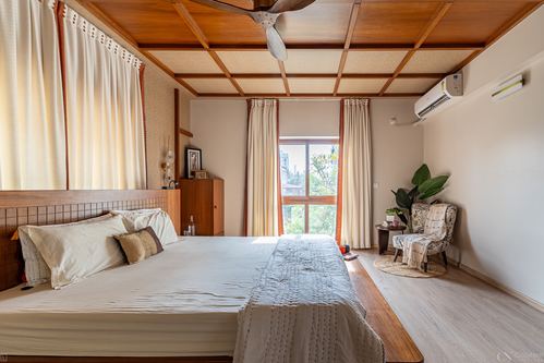 Bedroom with wood-beamed ceiling, bed against tiled headboard, and window seating corner
