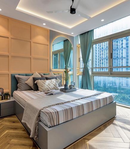 Bedroom with teal headboard, striped bedding, arched mirror, herringbone floor, and floor-to-ceiling city-view windows