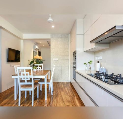Open galley kitchen with white glossy cabinetry beside a wood-floored dining nook