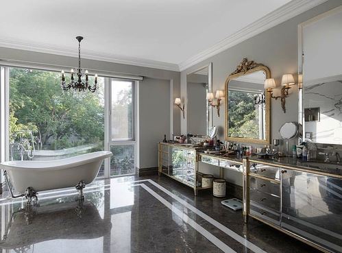 Marble bathroom with clawfoot tub by window and mirrored gold vanity beneath ornate mirror