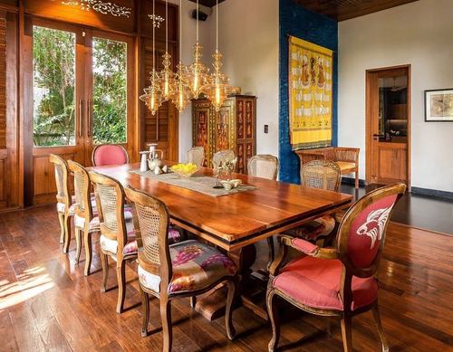 Long wooden dining table with cane chairs beneath cluster of glass pendant lights in traditional home