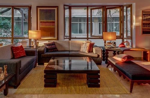 Warm-toned living room with dark sofas, low black coffee table, and large timber bay windows at dusk