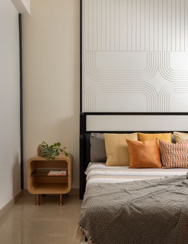 Bedroom with grooved paneled headboard wall, orange and mustard pillows, wooden rounded nightstand