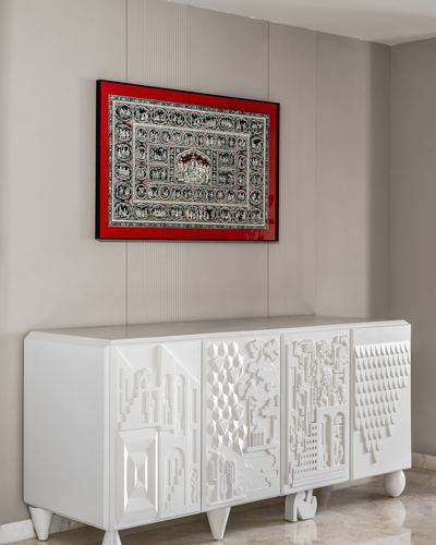 White carved sideboard below red-framed tribal artwork on grey wall