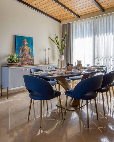 Dining room with oval table, navy velvet chairs, marble floor, and buddha painting above sideboard