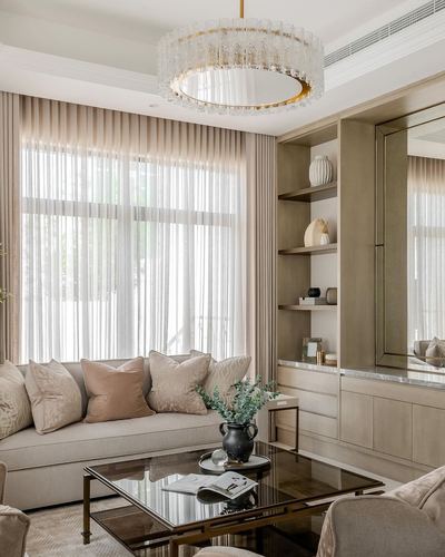 Beige living room with sheer curtains, crystal chandelier, built-in shelving and a pink-toned sofa