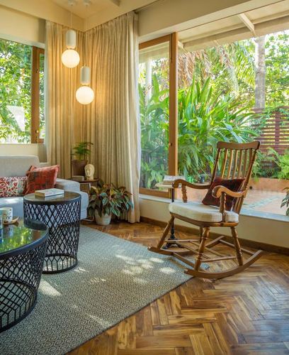 Living room with rocking chair, herringbone floor, and glass wall overlooking green garden