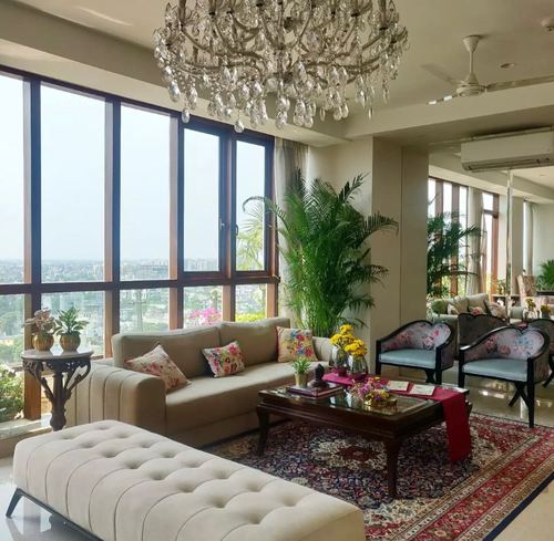 Living room with crystal chandelier, floral chairs, red carpet, and floor-to-ceiling city-view windows