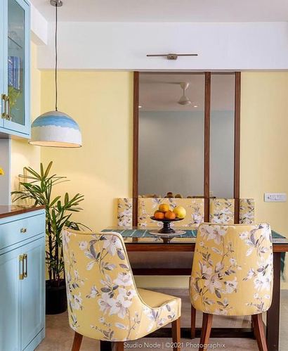 Yellow dining nook with floral chairs, blue cabinet, and dome pendant light