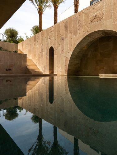 Sandstone courtyard wall with arched opening reflected in a still pool, palm trees above