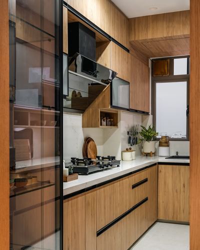 Wood-clad galley kitchen with white countertop, black hardware, and glass sliding pantry door in foreground