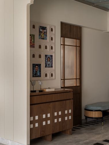 Foyer with arched niche gallery wall, wooden sideboard, and glazed panelled door beside marble flooring.