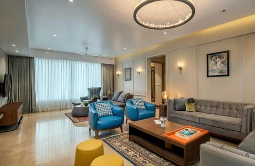 Living room with blue leather armchairs, grey sofas, wood coffee table and round chandelier