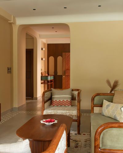 Living room with cane armchairs, wooden coffee table, and arched doorway leading to a wardrobe passage