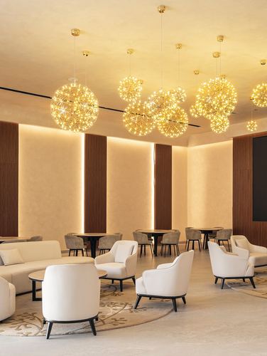 Lounge seating area with cream armchairs under clusters of glowing spherical pendant lights