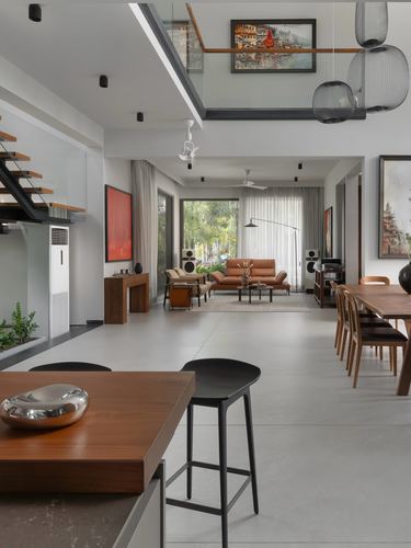Open-plan living and dining space with double-height ceiling, glass mezzanine bridge, and garden view beyond