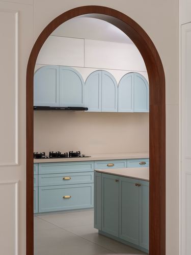 View through wooden arch into pastel blue kitchen with arched cabinet doors and island