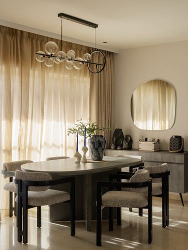 Dining room with oval table, black chairs, bubble chandelier, and sheer curtained window