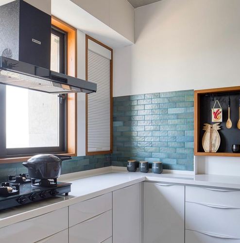 White kitchen corner with blue subway tile backsplash, chimney hood, and wood-framed window
