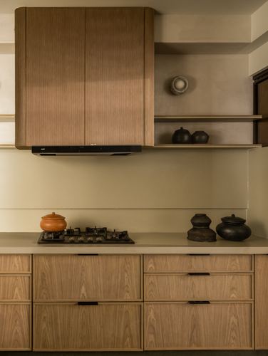 Kitchen counter with gas hob, terracotta pot, and ribbed wood chimney cabinet beside pottery on plaster shelves