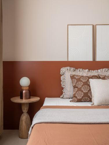 Bedroom corner with terracotta half-wall, patterned cushions, and a wooden pedestal side table with globe lamp